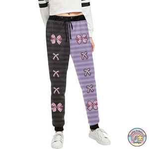 Op de afbeelding: Zwarte en paarse gestreepte sweatpants met roze strikken en een X-patroon.