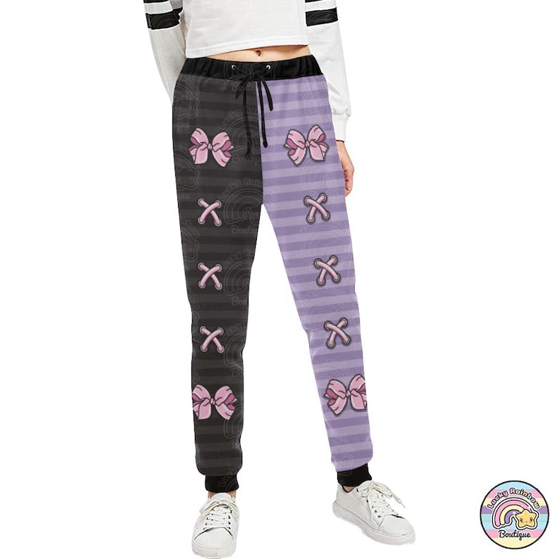 Op de afbeelding: Zwarte en paarse gestreepte sweatpants met roze strikken en een X-patroon.
