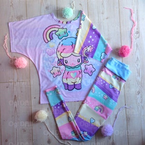 May include: A pastel pink and purple t-shirt featuring a rainbow and a cartoon sheep. The shirt is paired with matching leggings with a rainbow stripe pattern.