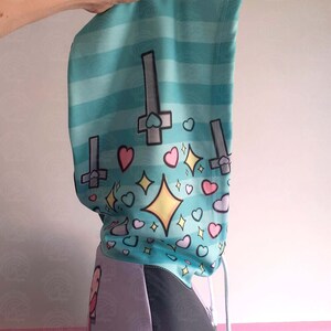 May include: A turquoise and purple hoodie with a graphic print of upside down crosses, hearts, and stars. The hoodie has a drawstring hood and a white drawstring.