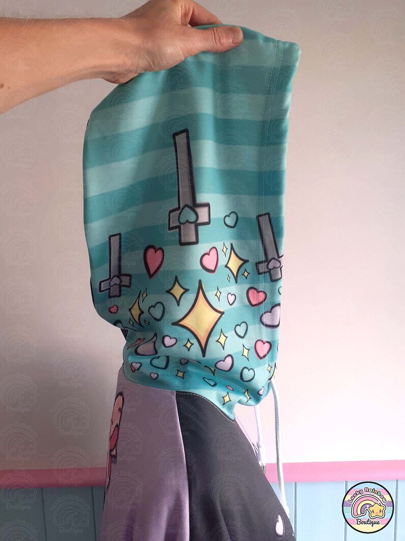 May include: A turquoise and purple hoodie with a graphic print of upside down crosses, hearts, and stars. The hoodie has a drawstring hood and a white drawstring.