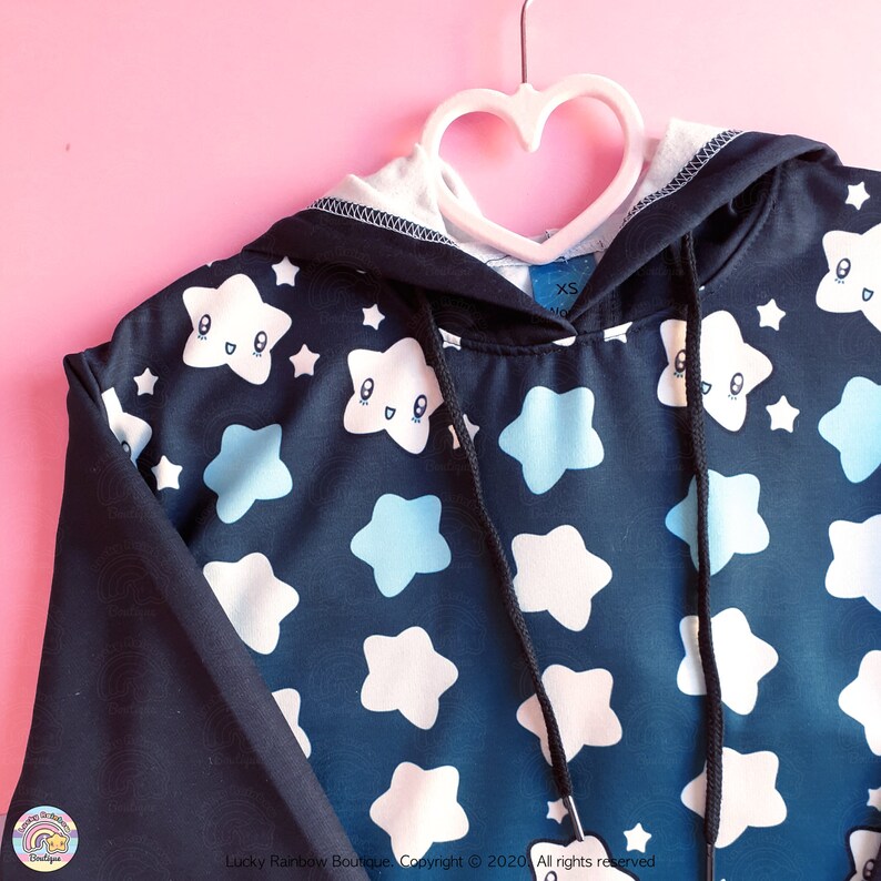 May include: Black hoodie with a blue and white star pattern. The stars have cartoon faces. The hoodie has a drawstring hood and a small tag that says "XS".