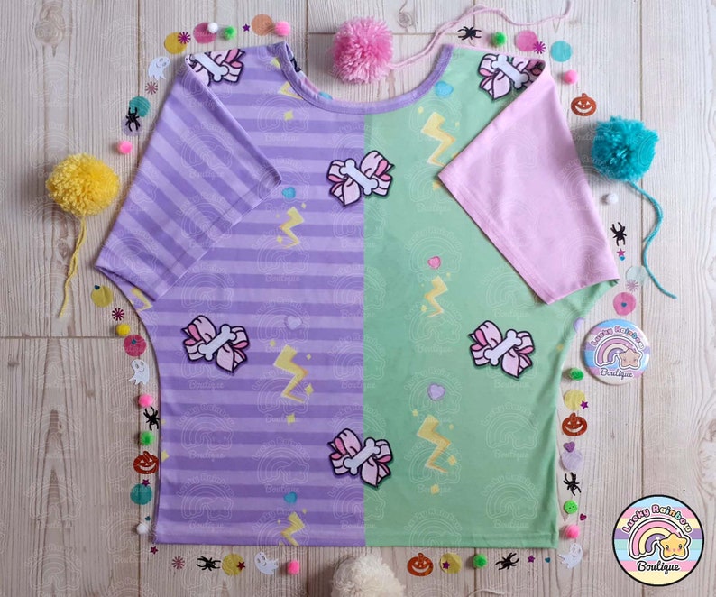 May include: A purple and green striped t-shirt with a pink bow and lightning bolt design. The shirt has a pink short sleeve on one side and a purple short sleeve on the other side.