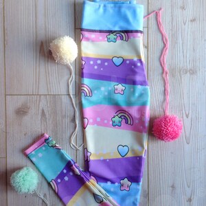 May include: A pair of colourful leggings with a rainbow, stars, and hearts pattern. The leggings are made of a stretchy fabric and have a blue waistband.