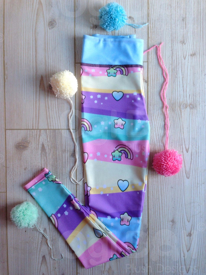 May include: A pair of colourful leggings with a rainbow, stars, and hearts pattern. The leggings are made of a stretchy fabric and have a blue waistband.