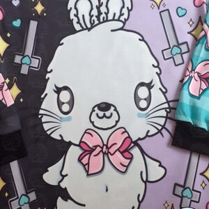 May include: A white bunny with pink bow tie and large eyes is on a purple background with a black and white background on the left side. The background has hearts, stars, and crosses. The text "Lucky Rainbow Boutique" is in the bottom right corner.