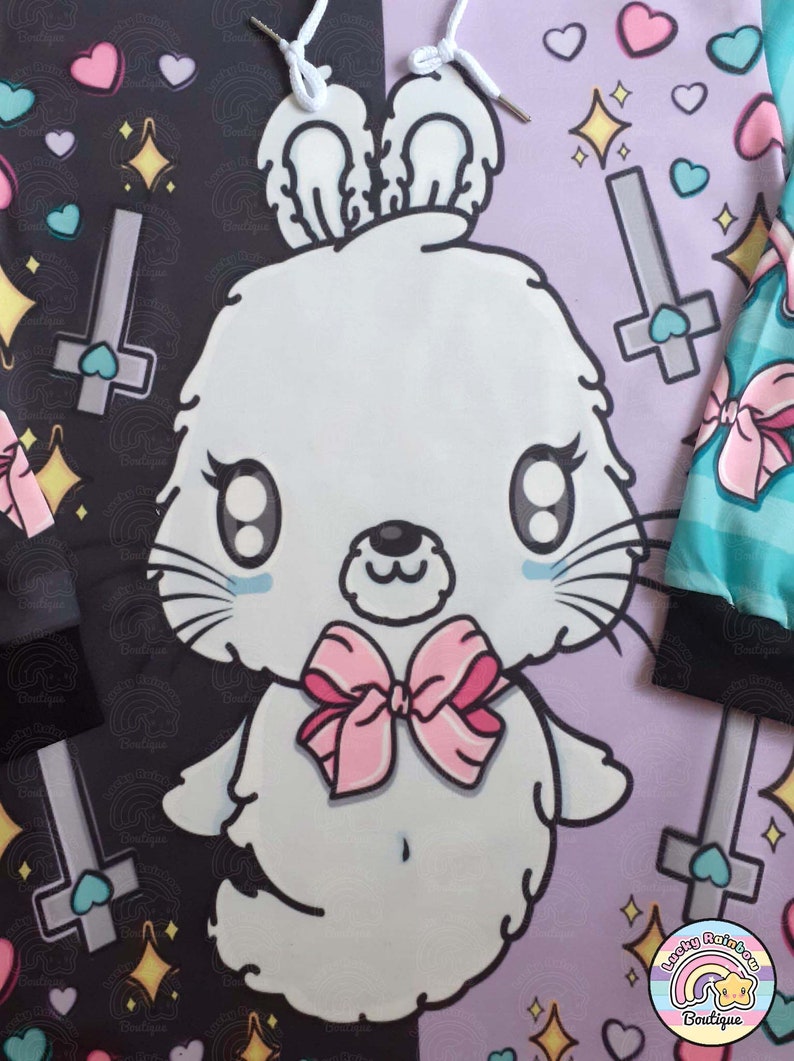 May include: A white bunny with pink bow tie and large eyes is on a purple background with a black and white background on the left side. The background has hearts, stars, and crosses. The text "Lucky Rainbow Boutique" is in the bottom right corner.