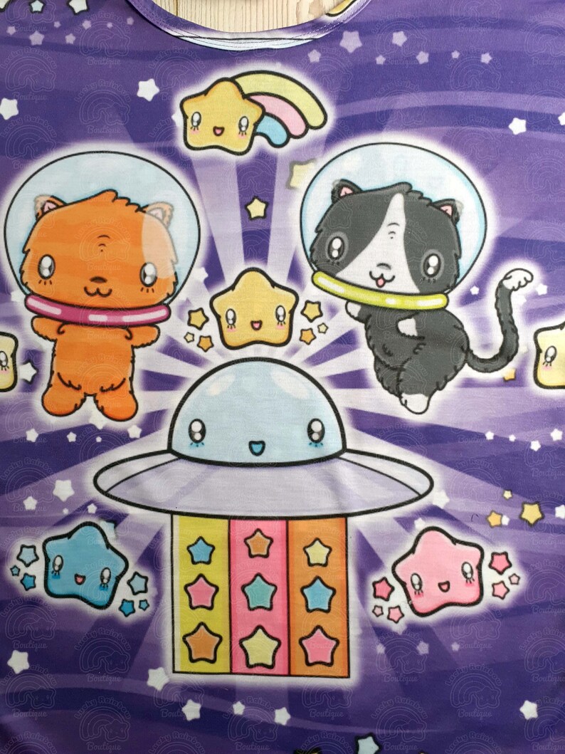 May include: A purple background with a cartoon spaceship, two cats in space suits, and stars. The spaceship is blue and white with a smiling face. The cats are orange and black with white faces. The stars are yellow, blue, pink, and orange.