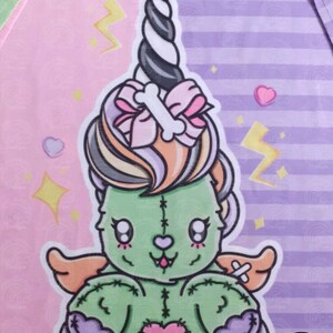 May include: A green stitched plush toy with a pink heart, wings, and a unicorn horn. The toy is sitting on a pink and purple striped background with stars and hearts.