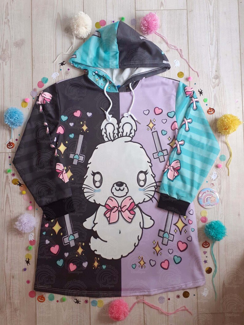 May include: A black and purple hooded sweatshirt with a white bunny rabbit design. The bunny has a pink bow and is surrounded by hearts, stars, and crosses. The sweatshirt has a split design with one side black and the other side purple.