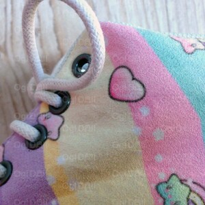 May include: Close-up of a light pink, blue, and yellow shoe with white laces and black eyelets. The shoe has a rainbow design with hearts and stars.