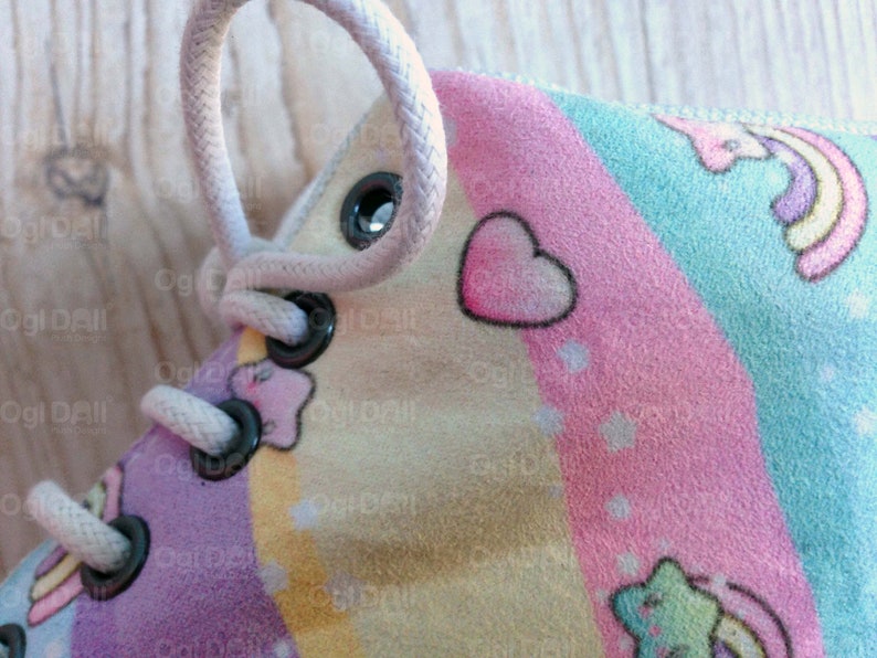 May include: Close-up of a light pink, blue, and yellow shoe with white laces and black eyelets. The shoe has a rainbow design with hearts and stars.
