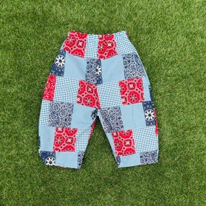 May include: Pants featuring a patchwork design composed of alternating fabric squares. The pattern includes red bandana prints, navy blue bandana motifs, and light blue and white gingham checks. The garment has an elasticized waistband.