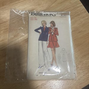 May include: A Butterick sewing pattern envelope in a clear plastic sleeve featuring illustrations of two outfits: a dark blue blazer with white wide-leg trousers, and a red patterned jacket with a matching skirt. Text includes Size 13 and Bust 35.