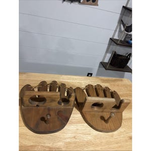 Peut inclure: Deux organisateurs muraux en bois en forme de gants de baseball. Chaque pièce présente une finition teintée brun foncé, une étagère centrale avec une découpe circulaire, un crochet à cheville saillant en bas et un laçage beige décoratif.