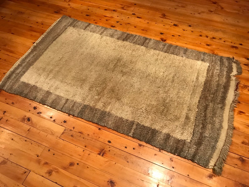 Puede incluir: Una alfombra rectangular verde claro con un borde verde oscuro y flecos. Se encuentra sobre un suelo de madera con un acabado c&aacute;lido y natural. La textura de la alfombra parece suave y afelpada, adecuada para un sal&oacute;n.