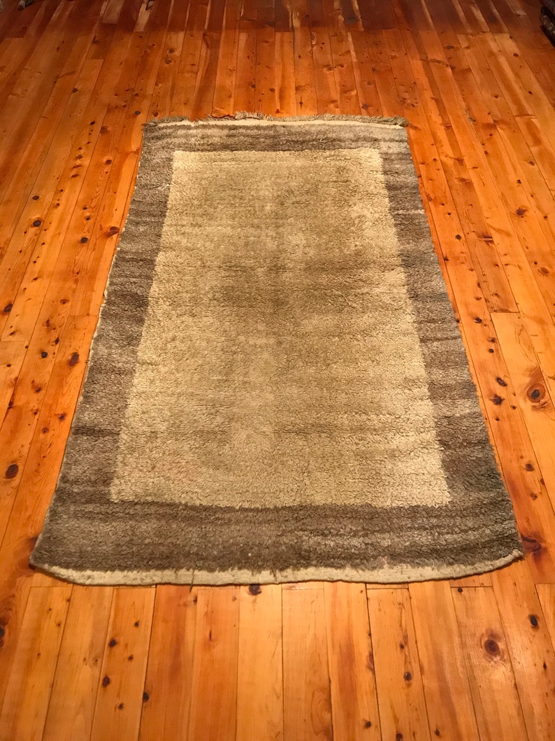 Puede incluir: Una alfombra rectangular con un centro verde claro y un borde verde oscuro. La alfombra est&aacute; colocada sobre un suelo de madera con vetas visibles.