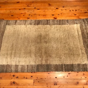 Puede incluir: Una alfombra rectangular con un centro verde claro y un borde verde m&aacute;s oscuro. La alfombra tiene una textura peluda y est&aacute; colocada sobre un suelo de madera. Los bordes de la alfombra tienen flecos.