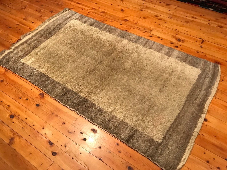 Puede incluir: Una alfombra rectangular con un centro marr&oacute;n claro y un borde marr&oacute;n m&aacute;s oscuro. La alfombra tiene un aspecto suave y texturizado y est&aacute; colocada sobre un suelo de madera con un tono c&aacute;lido marr&oacute;n rojizo. Los bordes de la alfombra est&aacute;n ligeramente deshilachados.