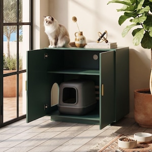 May include: A dark green wooden cat litter box enclosure featuring two hinged doors with gold handles, an arched side entry, and an open top shelf. A gray hooded litter box is placed inside the cabinet, which has a circular cord hole.