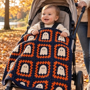 May include: A crochet baby blanket featuring a repeating pattern of white ghost motifs centered within orange and dark blue square granny squares. The blanket is draped over a child sitting in a stroller outdoors during autumn.