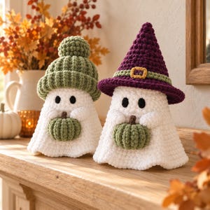 May include: Two white crochet ghost figures. The left ghost wears a sage green knit beanie and holds a small green pumpkin. The right ghost wears a purple pointed witch hat with a green band and gold buckle, holding a small green pumpkin.