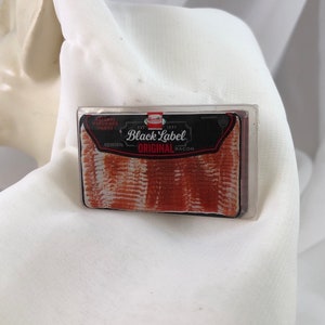 May include: A package of Black Label Original bacon. The package is rectangular with a black and red label. The bacon slices are visible through the clear plastic. The package is on a white surface.