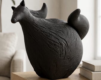 May include: A matte black ceramic sculpture of a stylized fox with a textured, bark-like surface. The fox is depicted in a seated position with its head turned to the side and a large, rounded tail curving upward behind its body.