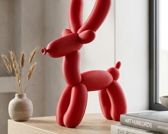May include: A bright red sculpture shaped like a balloon animal deer. The figure features elongated, smooth, rounded segments forming the head, long ears, a slender neck, a cylindrical body, four legs, and a small tail, all in a matte finish.