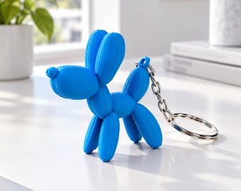 May include: A bright blue keychain shaped like a balloon dog. The figure features a textured, molded surface resembling twisted balloons, with a silver-toned metal chain and a circular split ring attached to the back of the dog's body.
