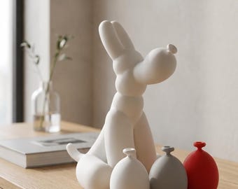 May include: A white ceramic sculpture shaped like a balloon dog, accompanied by three small, rounded vases in white, gray, and red. The dog figure has smooth, rounded limbs and a snout, while the three vases feature narrow necks and bulbous bodies.