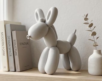 May include: A matte light gray sculpture shaped like a balloon dog. The figure features rounded, elongated segments forming the head, ears, body, and legs. It stands on a shelf next to three books titled Modern Form, Design Space, and Structure.