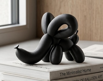 May include: A matte black sculpture shaped like an elephant made from twisted balloon forms. The sculpture is positioned on top of two stacked books, one titled The Minimalist Home and the other titled A History of Balloon Art, resting on a surface.