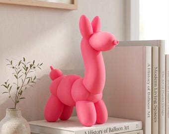 May include: A bright pink llama figurine crafted to resemble a balloon animal, featuring a smooth, matte finish. The llama stands on a stack of three books titled A History of Balloon Art, Modern Living Spaces, and The Art of Plaster Design.