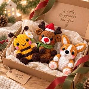 May include: A cardboard gift box containing three crocheted stuffed animals: a yellow and black bee with a white flower, a brown reindeer with a red Santa hat and green scarf, and a tan and white corgi. The box lid reads A Little Happiness For You.