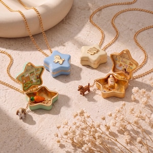 May include: Three star-shaped locket necklaces with gold chains. One is light blue with a dog charm, one is mint green with a rabbit charm and carrot, and one is cream with a dachshund charm and a small bottle. Each opens to reveal a pet shop scene.