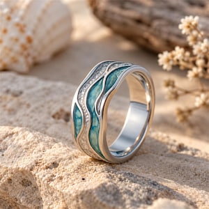 May include: A silver-toned ring featuring a wavy, multi-layered design. The band incorporates smooth, teal-colored enamel sections that mimic flowing water, contrasted with textured, shimmering silver-toned inlay details.