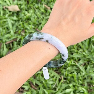 以下が含まれることがあります： 半透明の白と深いフォレストグリーンの鉱物インクルージョンが混ざり合ったマーブル模様の、滑らかで丸みを帯びたバングルブレスレット。円形のアクセサリーは光沢のある磨き上げられた仕上げで、小さな空白の白い長方形のタグが付いています。