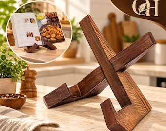 May include: A dark brown wooden book stand constructed from two interlocking pieces of wood forming an X-shape. The stand features a visible wood grain texture and angled supports designed to hold an open cookbook or tablet in an upright position.