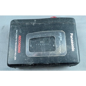May include: A black Panasonic RQ-L309 mini cassette recorder featuring a central transparent window with a scale and direction indicator. The device has white text labeling it as a recording unit with fast playback functionality.