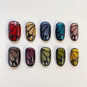 May include: A set of ten press-on nails arranged in two rows, each featuring a butterfly wing pattern with black veins and white dots. The colors include red, yellow, dark blue, teal, pink, grey, purple, olive green, lime green, and mustard.