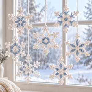 May include: Six hanging snowflake ornaments crafted from white and light blue yarn. Each snowflake features a central star-shaped pattern with intricate crochet detailing, suspended by thin white strings against a window pane.