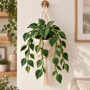 May include: A crocheted hanging plant featuring vibrant green leaves in a cream-colored pot held by a macrame hanger. The plant has multiple trailing vines with heart-shaped leaves, and the pot is suspended by knotted off-white cord.