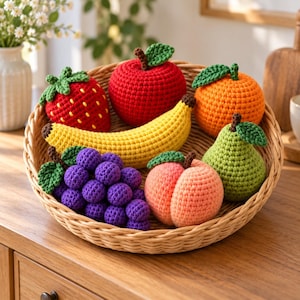 Peut inclure: Un ensemble de fruits au crochet dans un panier rond en osier, comprenant une fraise rouge à graines jaunes, une pomme rouge, une banane jaune, une grappe de raisin violet, une orange, une pêche et une poire verte, chacune avec une feuille.