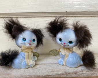 May include: Two blue ceramic kittens with brown fur accents. The kittens have painted eyes, pink noses, and yellow bows.