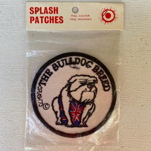 May include: A round patch featuring a bulldog wearing a Union Jack vest, with the text "THE BULLDOG BREED" around the edge. The patch is in a clear plastic package with the words "SPLASH PATCHES" at the top.