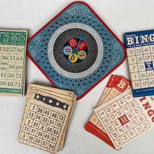 May include: A collection of vintage bingo game components. Includes bingo cards, a blue and red bingo cage, and bingo number markers. The cards are printed with numbers and the word "BINGO".