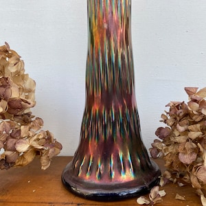 May include: A tall, iridescent glass vase with a textured, ribbed surface. The vase is a deep purple, blue, and green color with a metallic sheen.