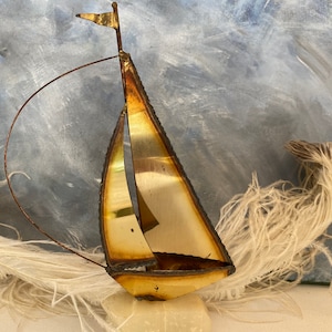 May include: A gold metal sailboat sculpture with a white feather plume in the background. The sailboat has a single sail and a small flag at the top.