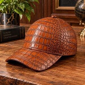 May include: A brown baseball cap featuring a textured crocodile skin pattern. The cap has a structured crown and a curved brim, with a button at the top centre. The material has a glossy finish that highlights the embossed scale details throughout.